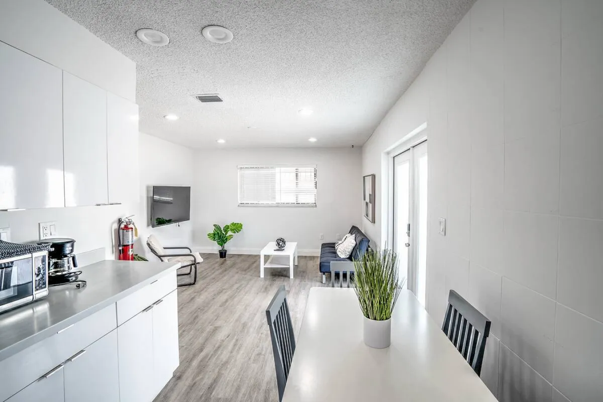 An inviting open-plan area combining a comfortable seating space, kitchen countertop, dining table, and lush indoor plant. The interconnected layout is ideal for entertaining, cooking, or relaxing with loved ones.